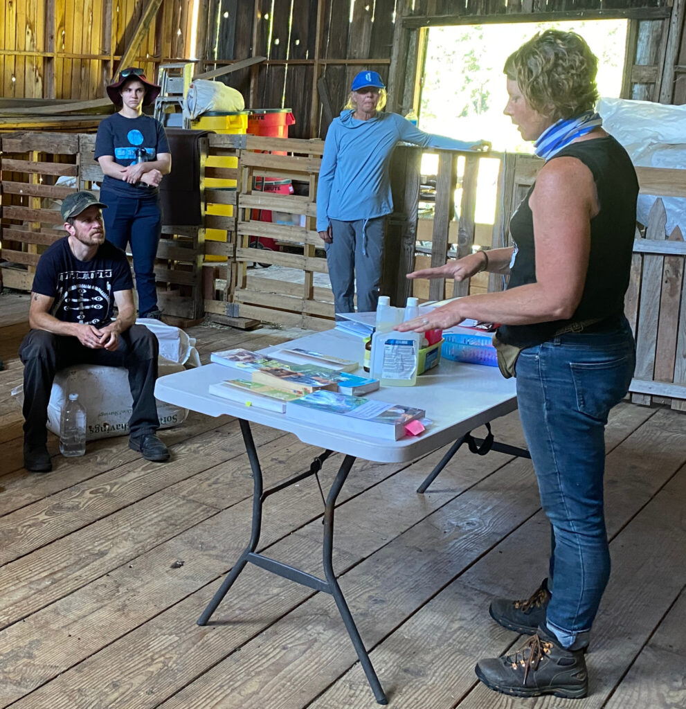 Roni stands before a table covered in various medical equipment and books and discusses how they help her administer ruminant care. 