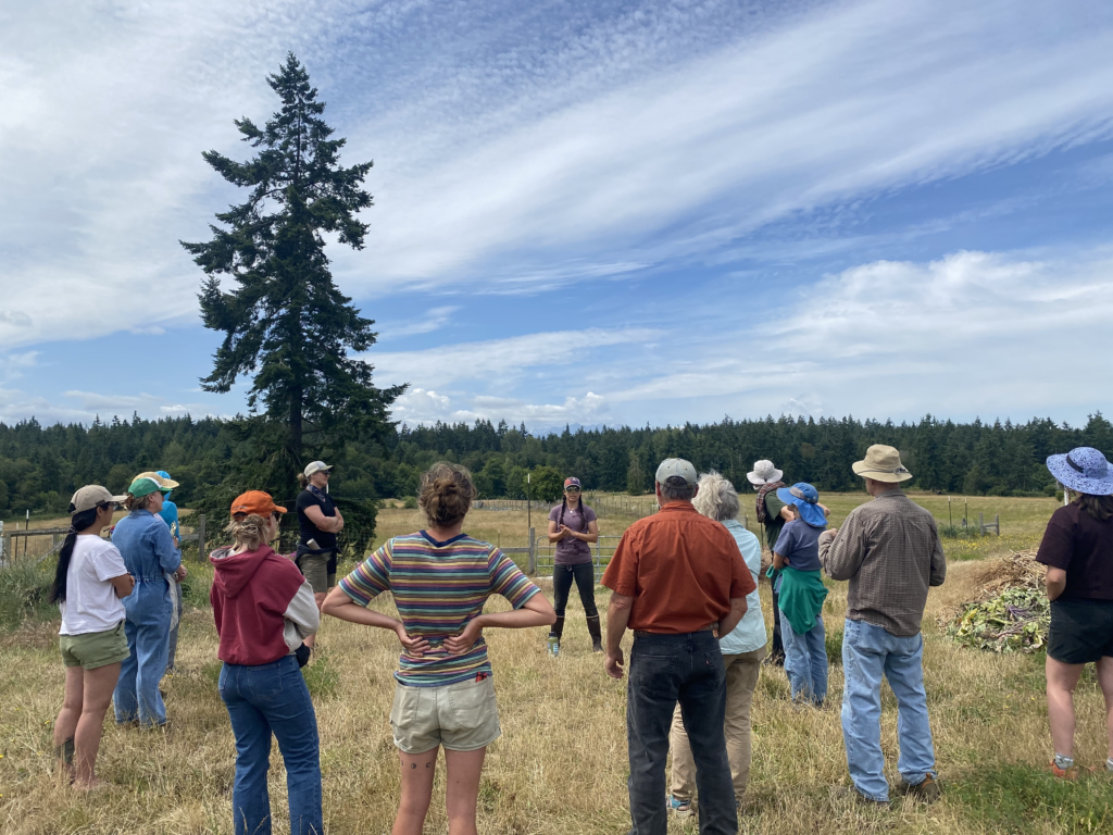 Class participants stand in a circle and listen to farmer Hailey speak about native hedgegrow plants 
