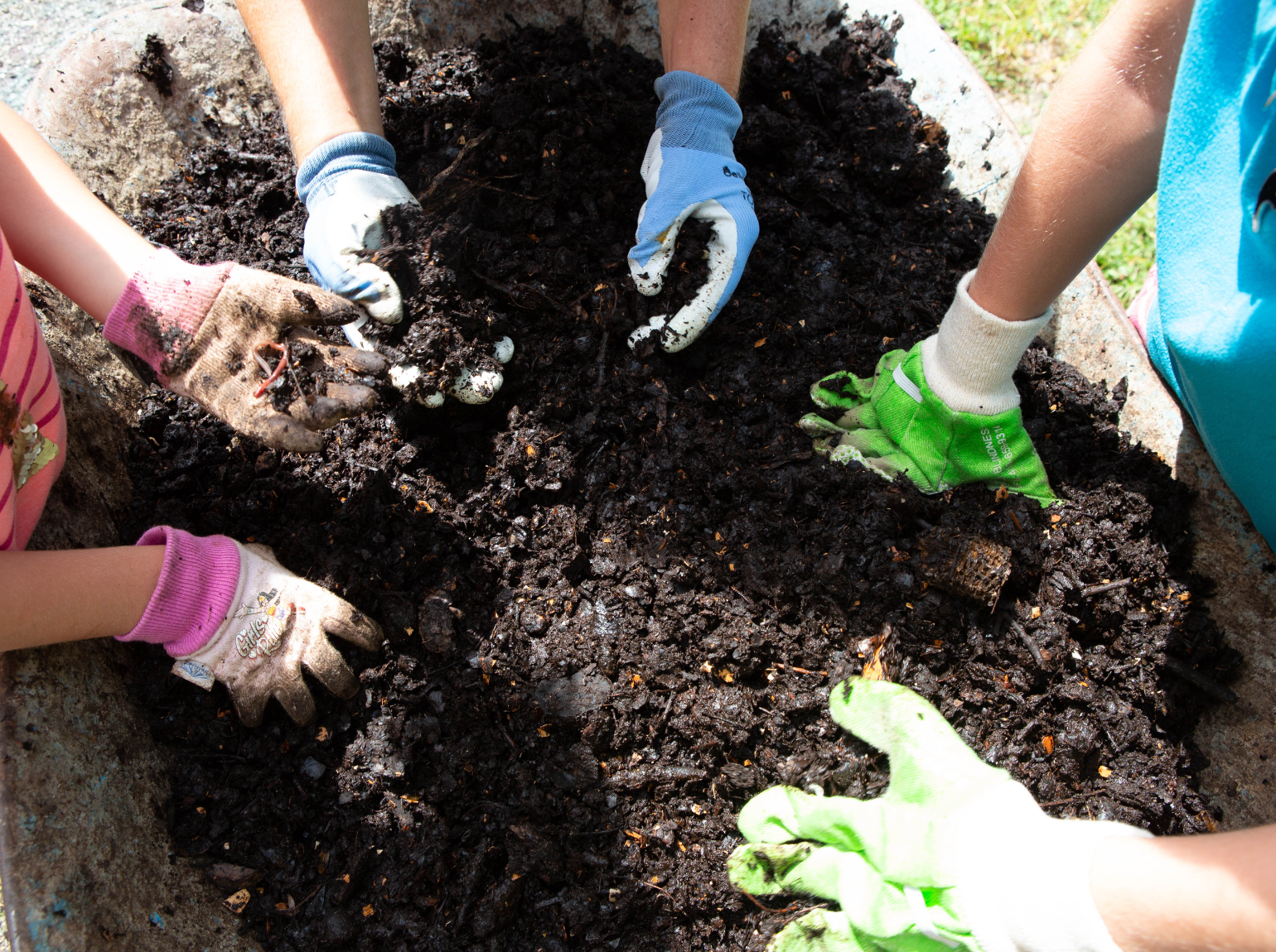 3 people wearing gardening gloves gather around a pile of fully composted soil.