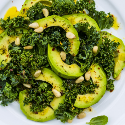A salad consisting of kale, avocado, sunflower seeds, and dressing on a white plate.