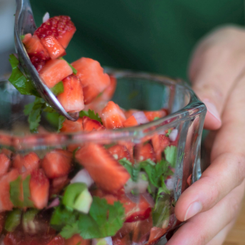 someone stirring a strawberry salsa in a glass bowl