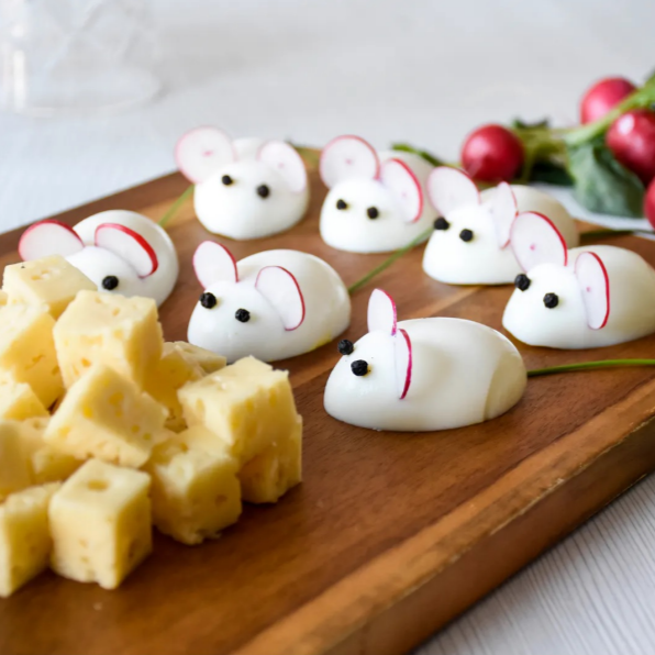 Egg halves shaped as mice with radish ears, looking at a pile of cheese