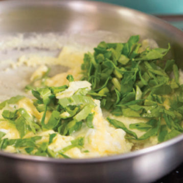 scrambled eggs with a pile of greens on top in a pan