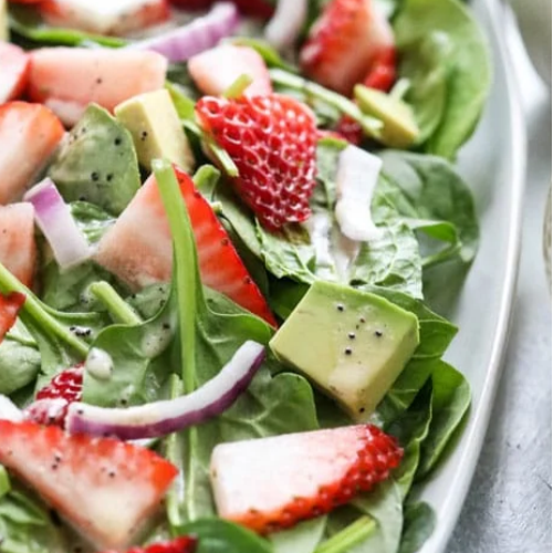 Close up of a salad with strawberries, avocado chunks, onion, and dressing