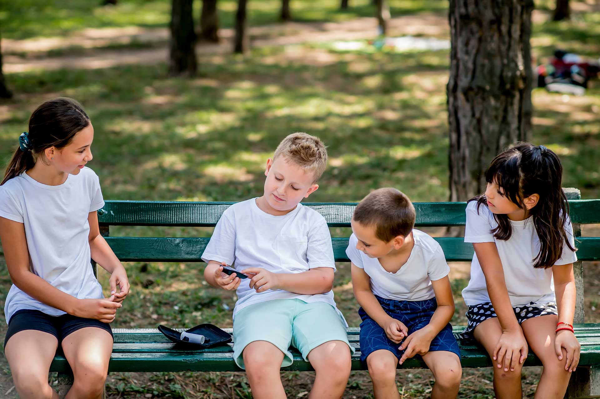 three children watching fourth check his blood glucose