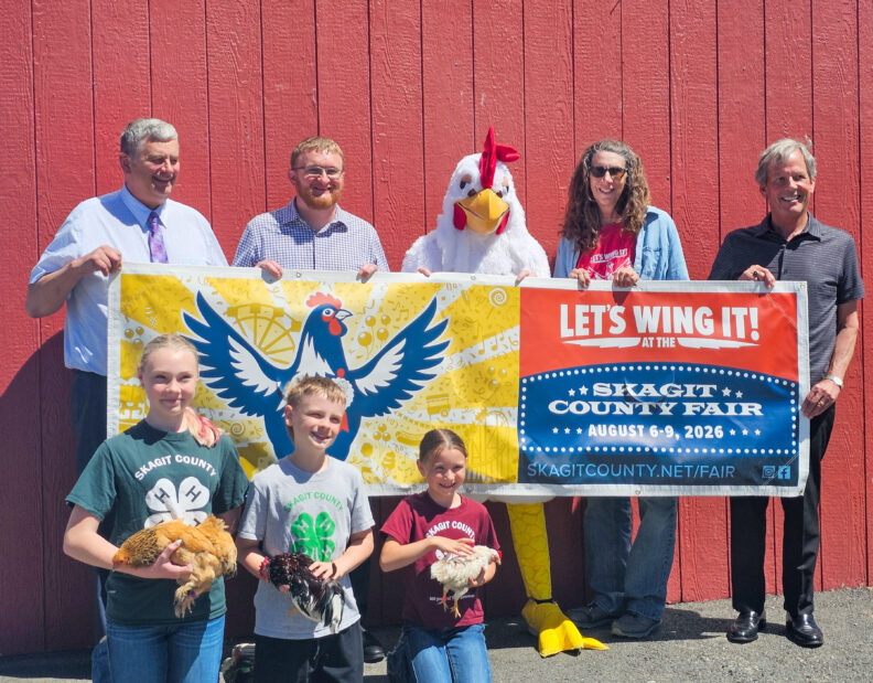 Skagit County Commissioners holding "Let's Wing It" Banner with 4-H youth members and chickens. 