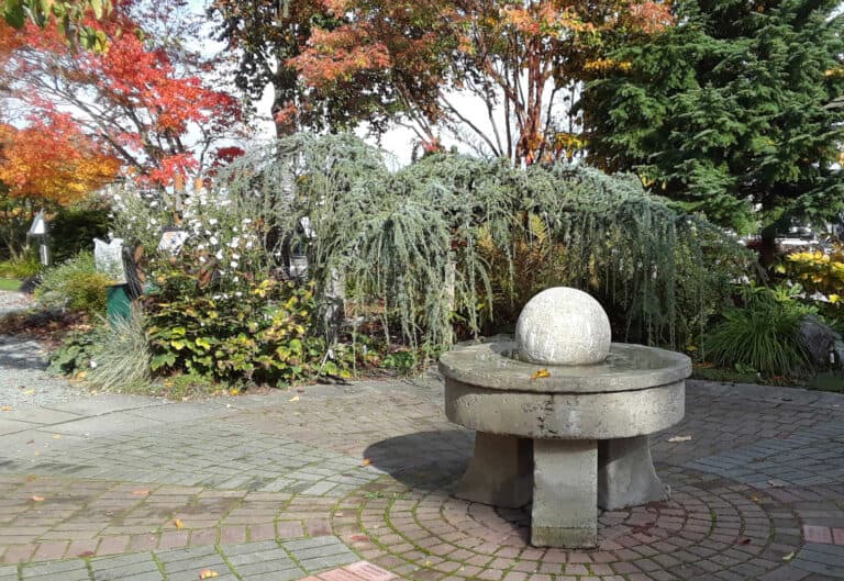 Picturesque entry garden with a fountain, shaded by trees, inviting visitors to enjoy the view.
