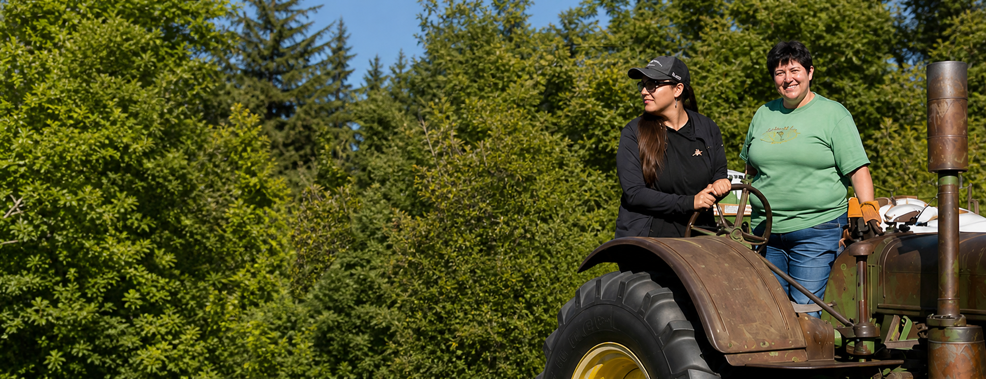 Two women on a tractor with evergreen tree backdrop