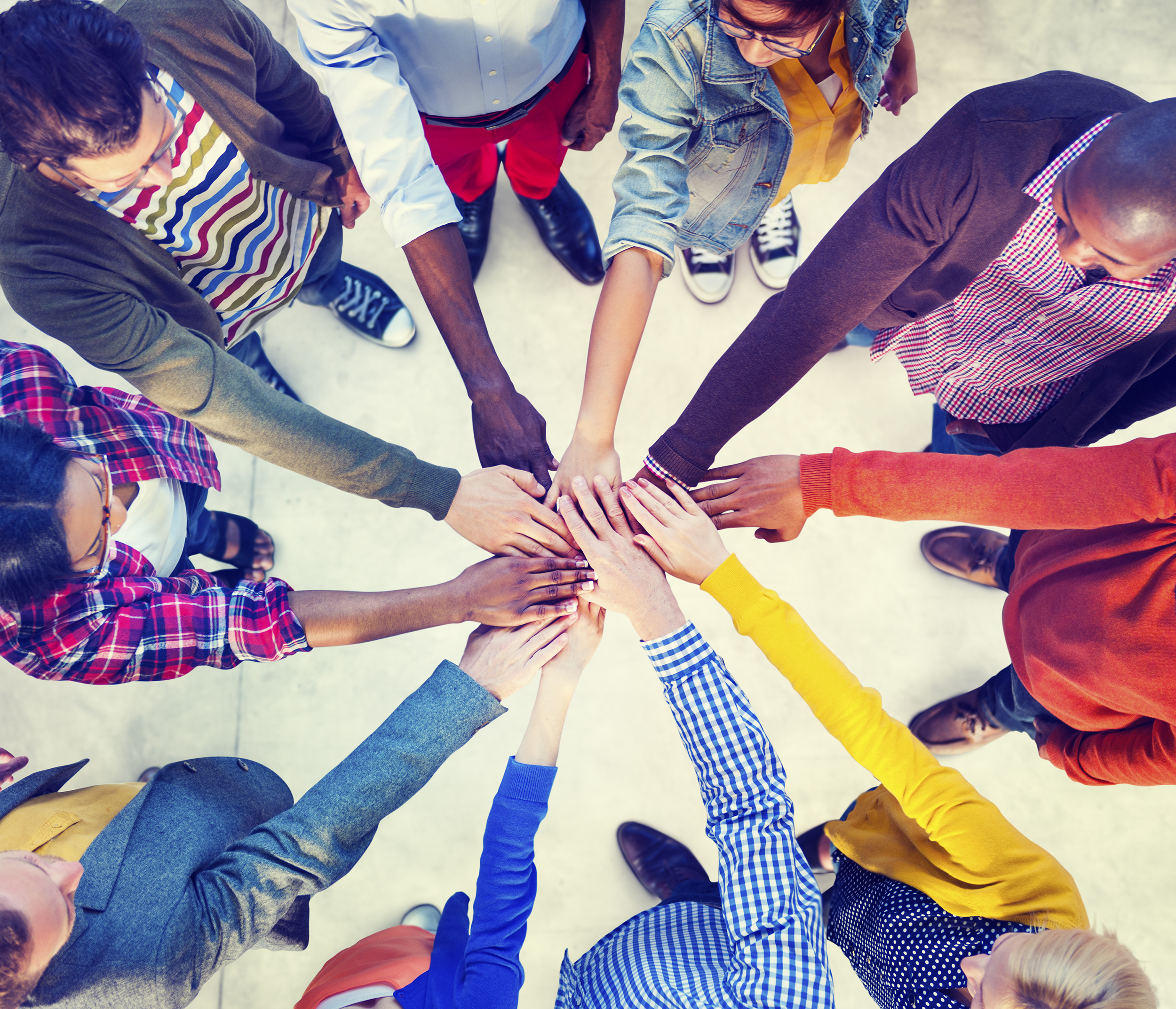 Group of people standing in a circle with hands placed in center of the circle symbolizing team work.