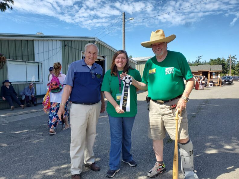 Three people with large ribbon at fairgrounds