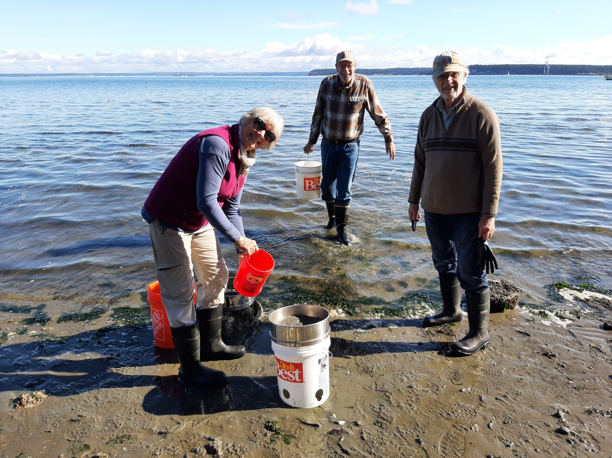 Three people at water's edge with buckets of water