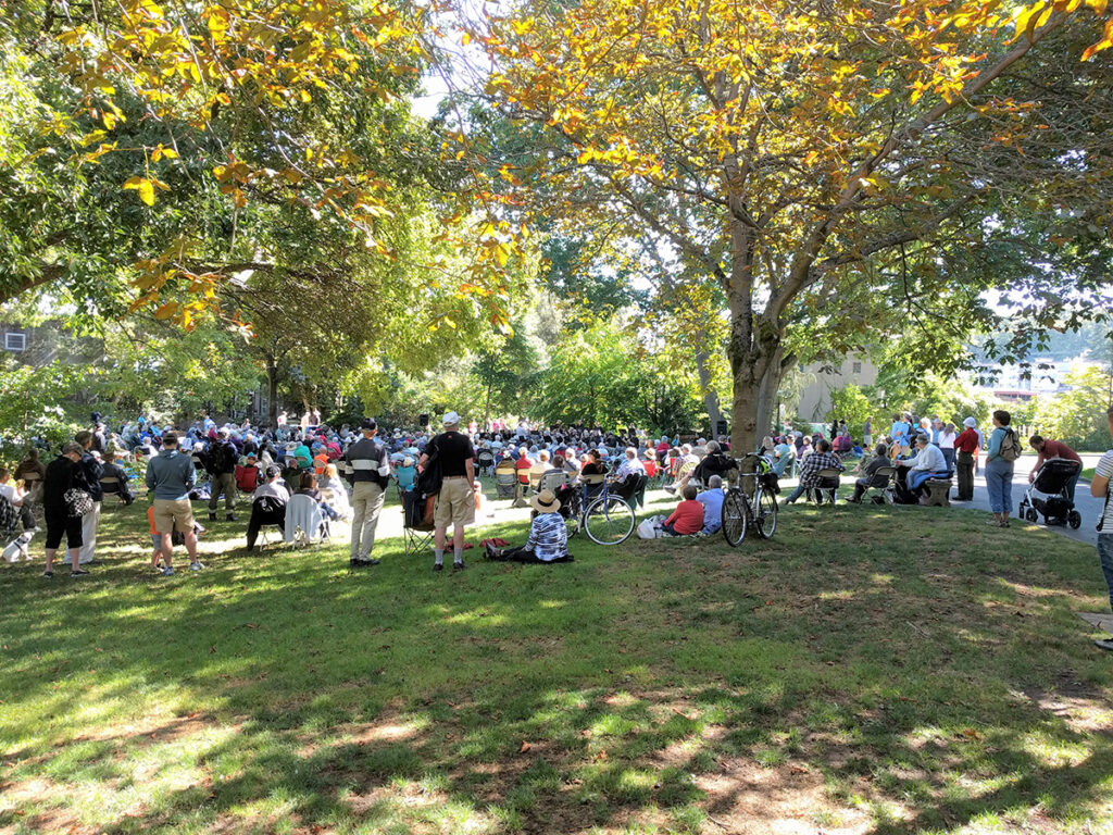 A large group of people congregating in shade in a public space.