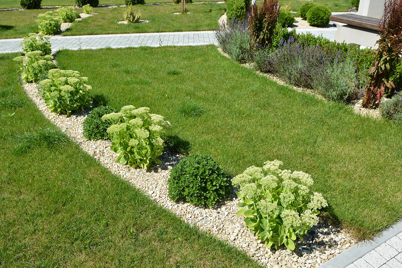 A landscaped lawn with neatly trimmed grass, stone-edged garden beds, and ornamental plants.