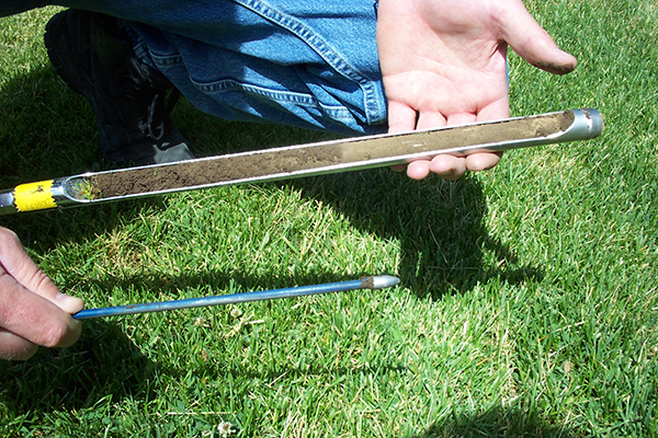 Person holding a soil probe and a tile probe over grass, showing about six inches of soil moisture penetration depth.