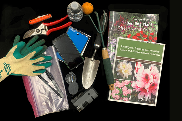 Collection of horticultural tools and materials arranged on a black background, including gardening gloves, pruning shears, a soil trowel, a hand cultivator, a notepad, a smartphone, permanent markers, a magnifier, plastic bags, reference books on plant diseases and pests, a water bottle, and an orange.
