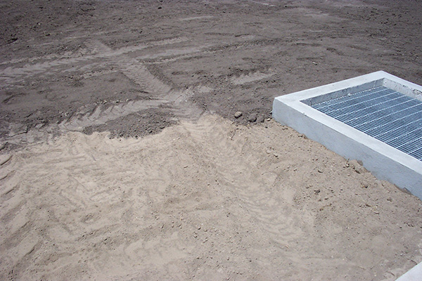 A thin layer of darker soil abuts a layer of lighter-colored soil. Heavy machinery tread is apparent in both layers.