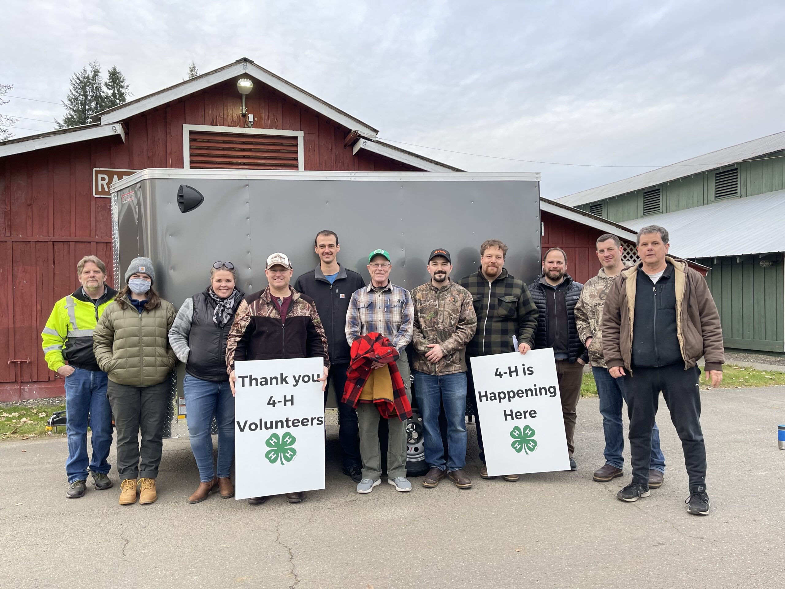 Group of 4-H volunteers holding 4-H volunteer signs in front of trailer.