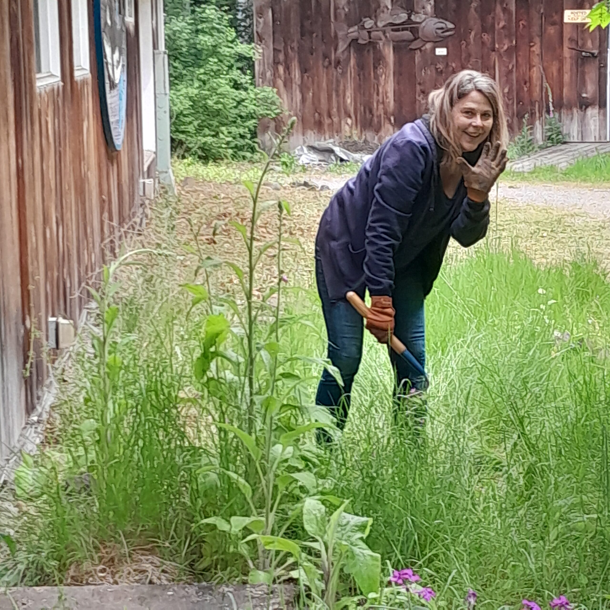 Master Gardener Jodi Koch smiling and waving at the camera while weeding.
