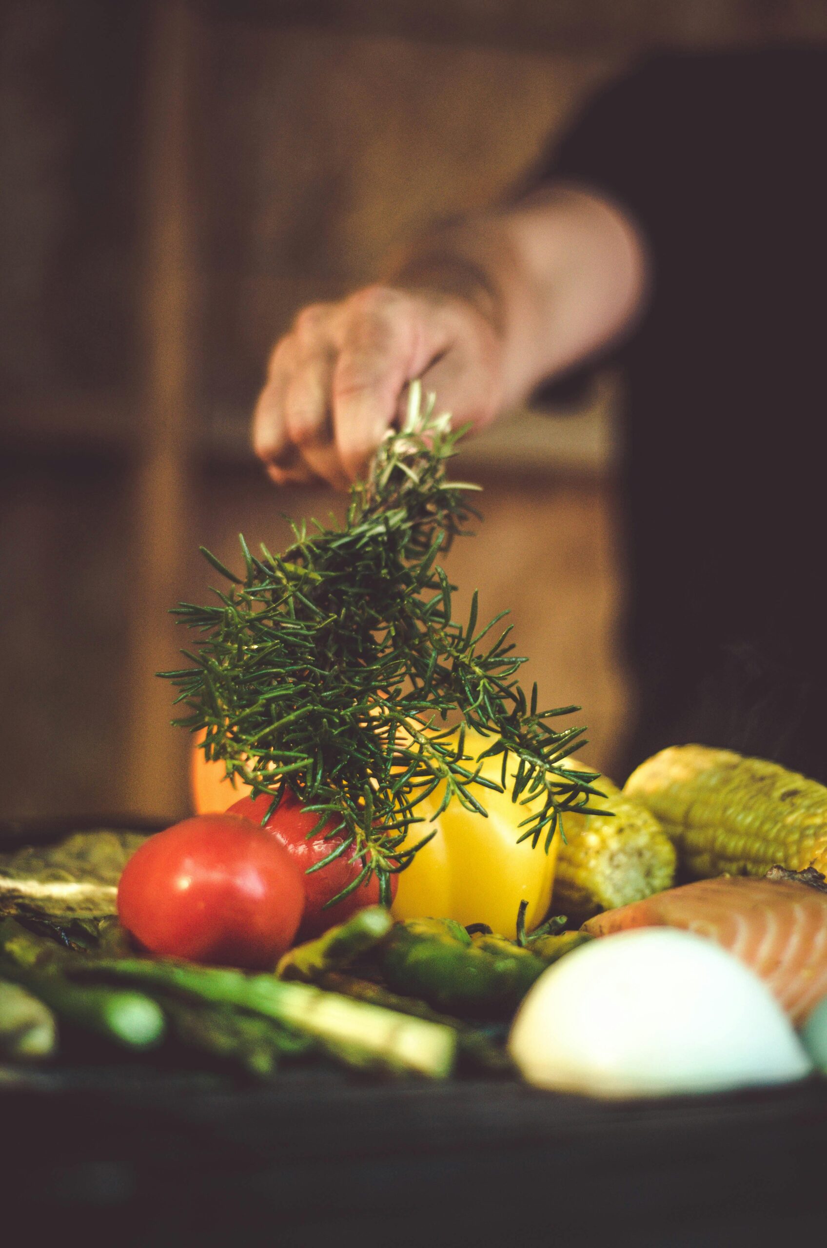 Person adds rosemary to pan of chopped vegetables.