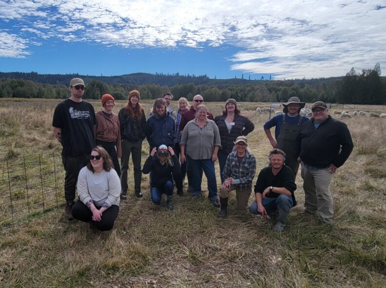 CS in-person intensive attendees from 2024 class standing in a field facing camera.