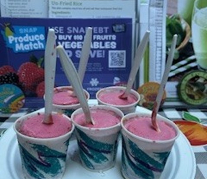 Green and white paper cups filled with pink yogurt with sticks in the center and sitting on a white plate.