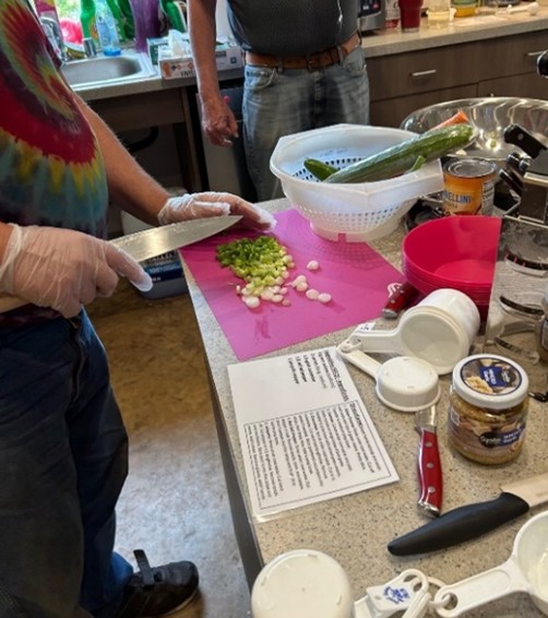 Resident at Veterans Village slicing vegetables on pink cutting board.