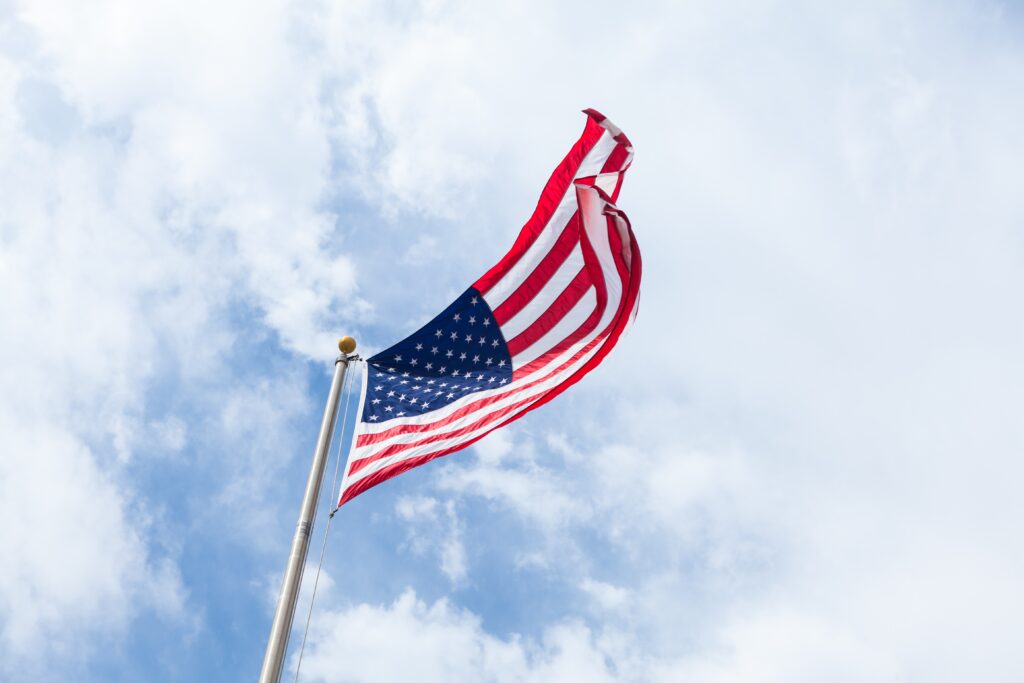 Image of a United States Flag waving in the wind with blue sky with clouds in background 