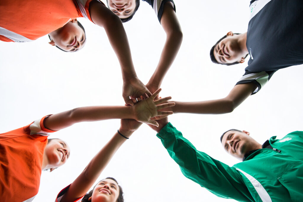Image of several teens in a circle with hands connecting in the center of the image 
