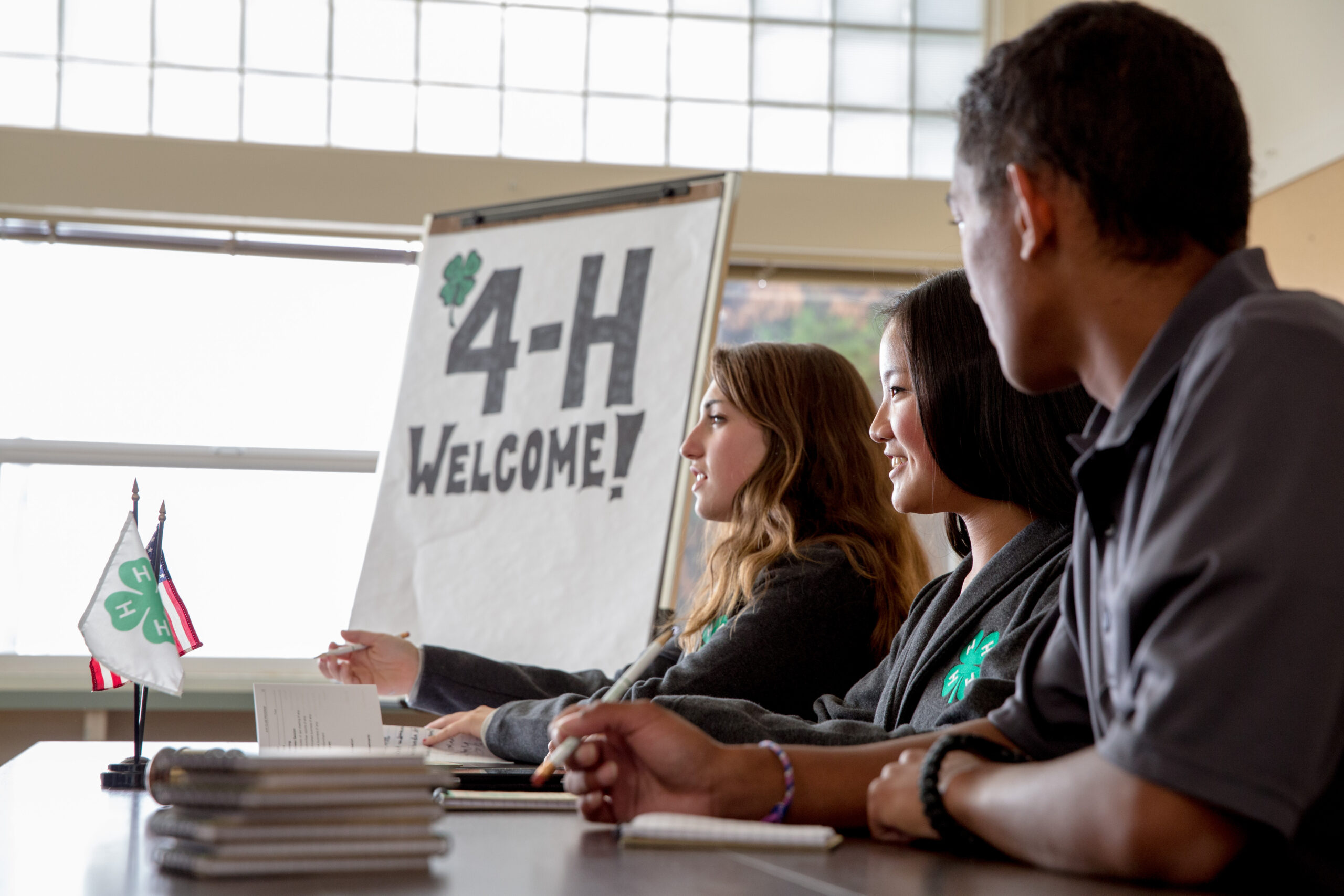 Three people sitting at a table with a sign that reads, "4-H Welcome!"