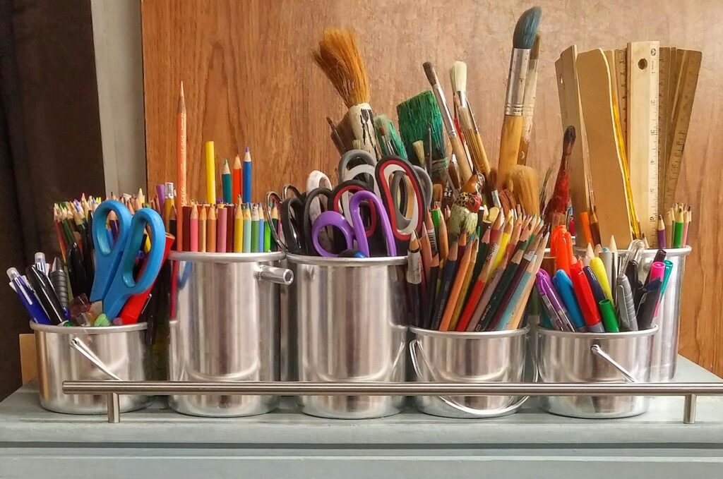 image of cans of pencils, pens, scissors, paint brushes and rulers