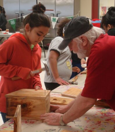 Adult mentor teaching youth to build a birdhouse using hand tools.