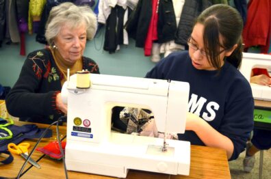Adult mentor teaching a youth to use a sewing machine.