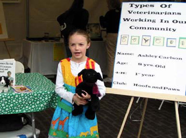 Young girl, holding stuffed animal and standing in front of her poster, giving a speech on types of veterinarians.