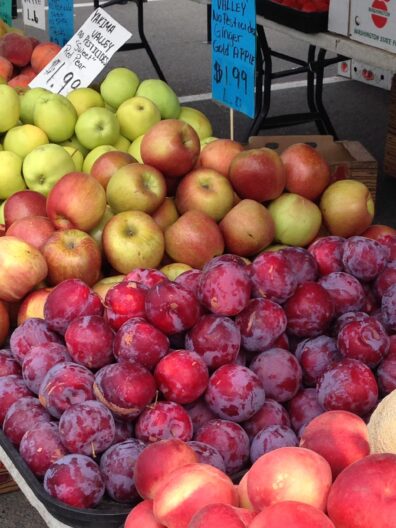 Peaches, plums, and apples arranged for sale at a farmers market.