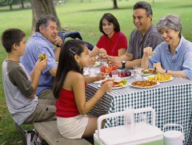 Family enjoying a picnic together at a park table with food and drinks.