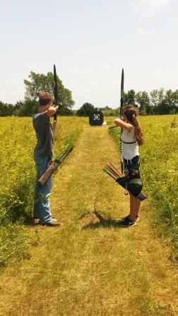 Boy and girl 4-H teen archers, aiming at a distant target in a field.