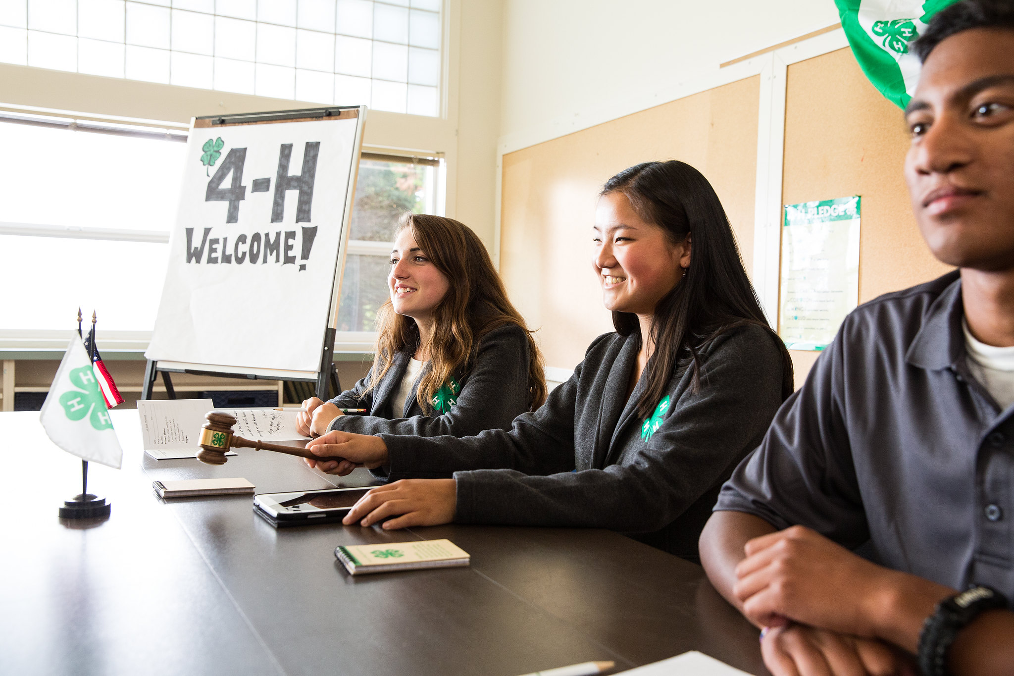 Teens sitting at head table with 4-H Welcome! sign.