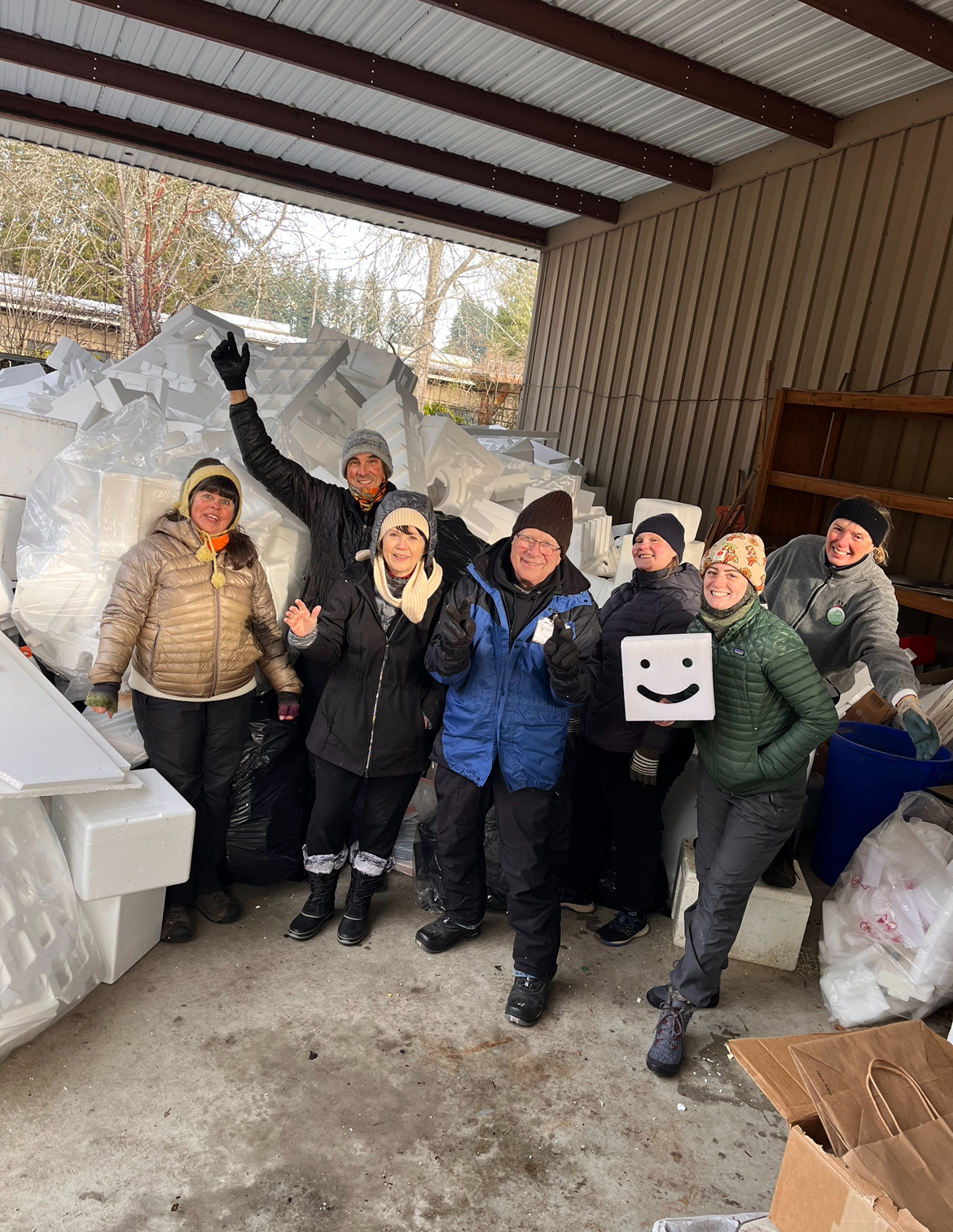 Group of people smiling in front of a large pile of Styrofoam.