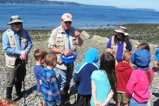 Two beach naturalists teaching a group of children on the beach.