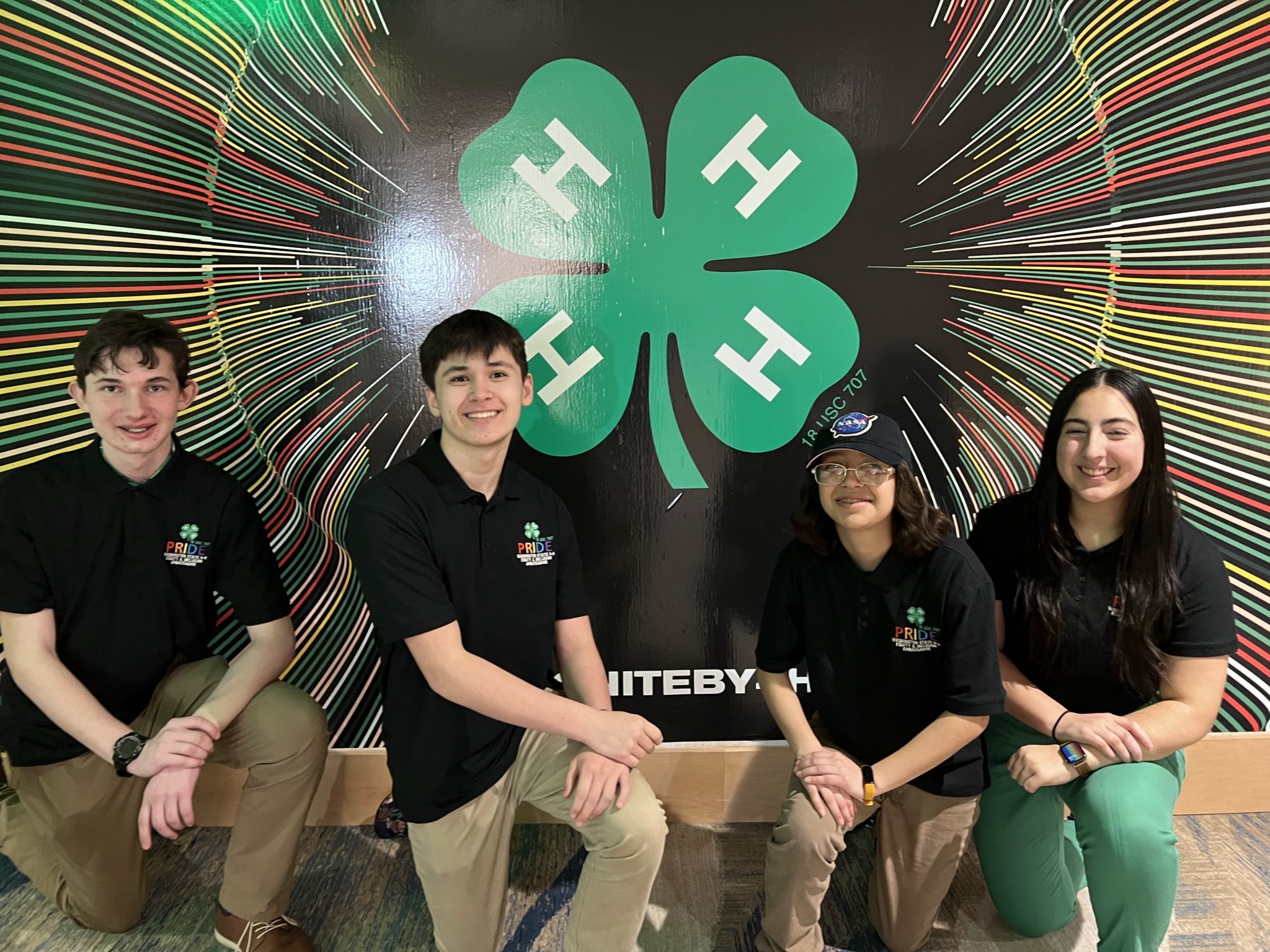 Four teens in front of a 4-H Clover.