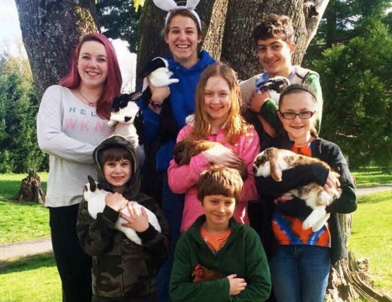 Group of smiling kids outdoors holding rabbits and a chicken in front of a tree.