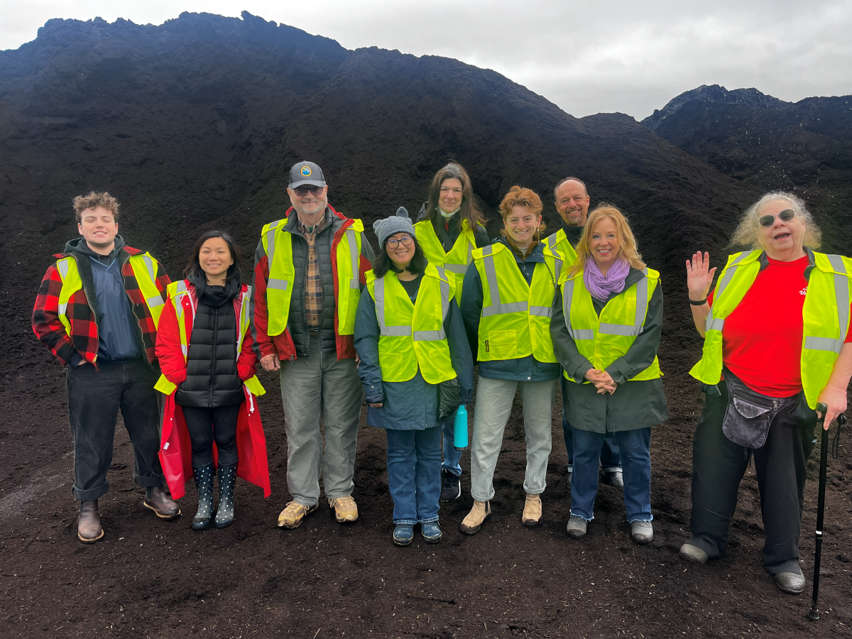 Group of smiling volunteers in high visibility vests posing in front of a pile of compost.