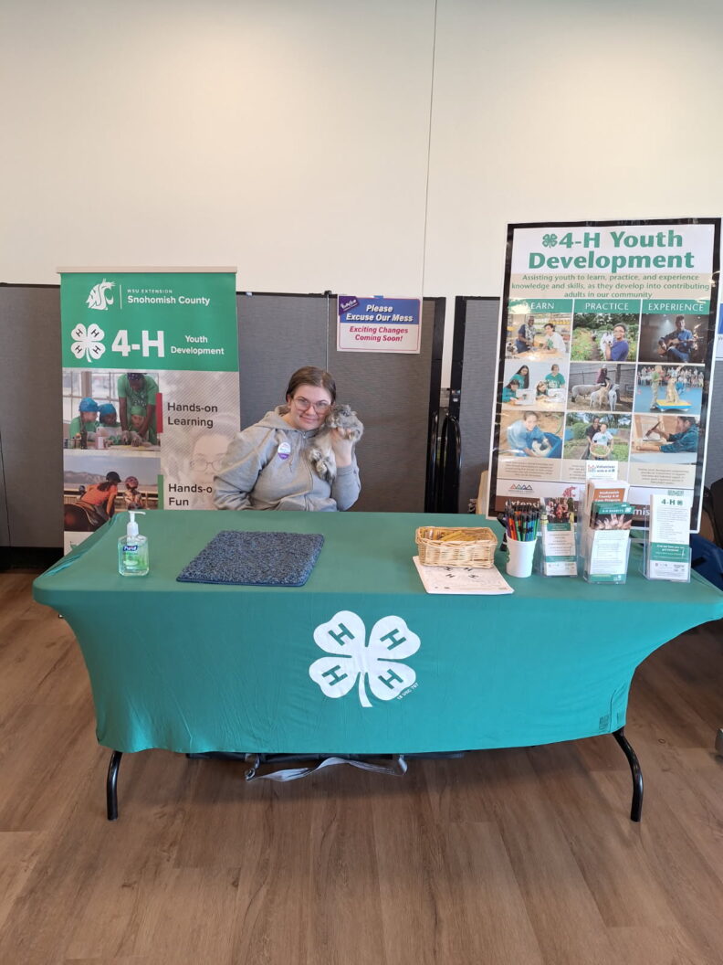 4-H member with rabbit at outreach table for public event; banners and 4-H decorations, give-aways.