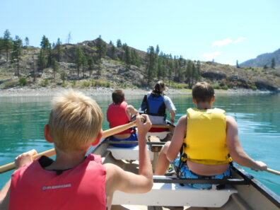 Four children in a canoe in life jackets on a lake.
