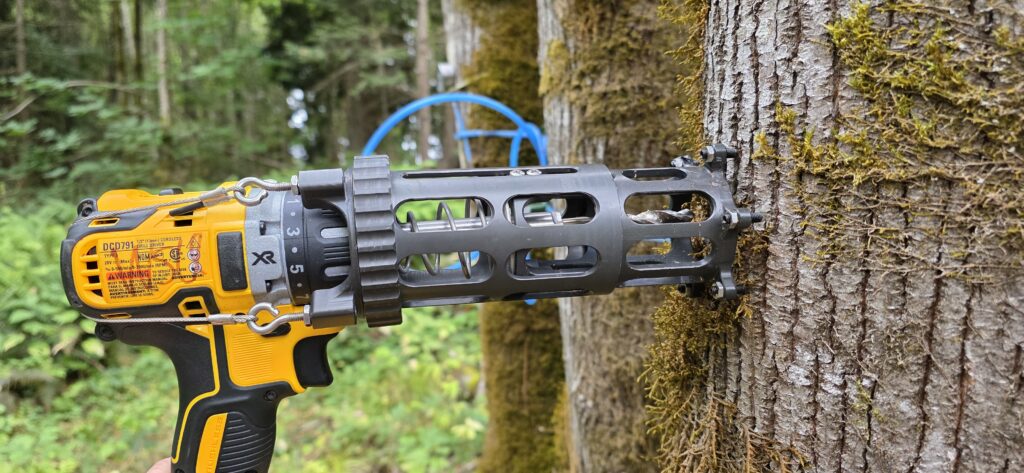 A handheld drill with a precision tapping frame installed set against tree.