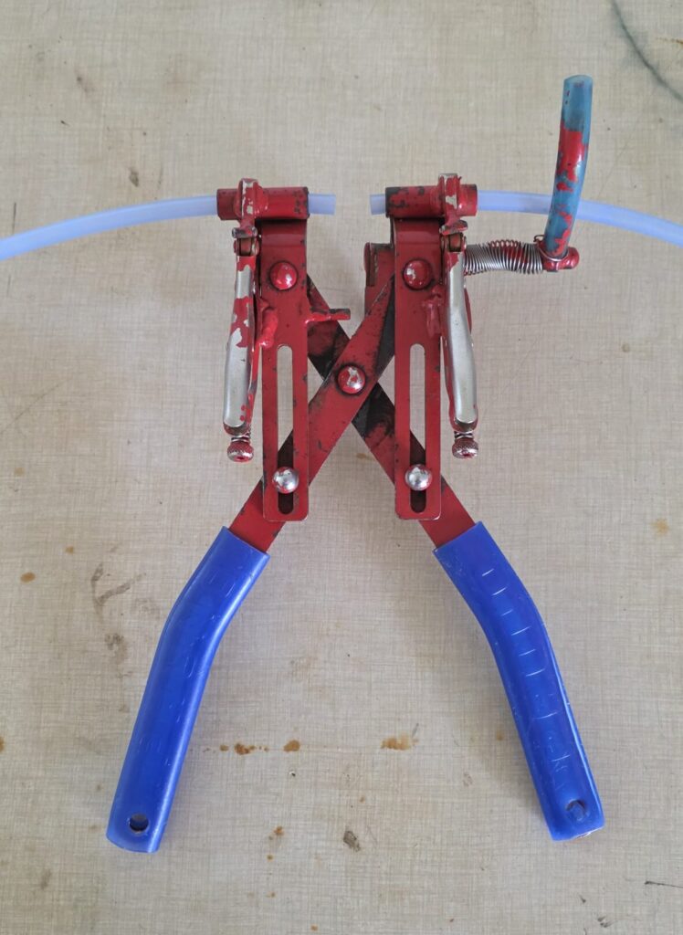 A pair of red and blue dropline pliers with tubing in the vice grips.