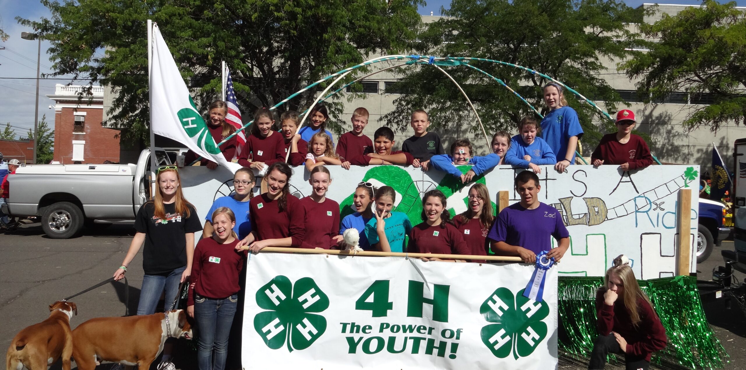 Group of youth holding 4-H banner in front of 4-H fair parade float.