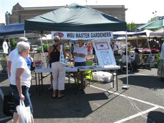 Farmers market booth with WSU Master Gardeners talking with shoppers