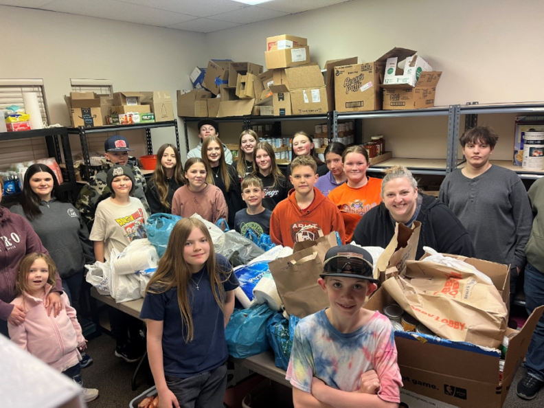 A group of youths and their 4-H leader posing in a food pantry.