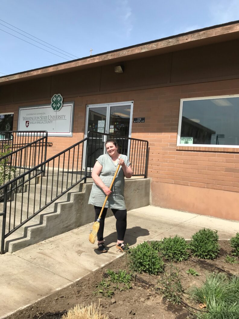 WSU staff person holds a broom next to the demonstration garden
